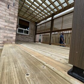 Covered wooden deck with transparent pergola roofing and privacy screens in a residential backyard.