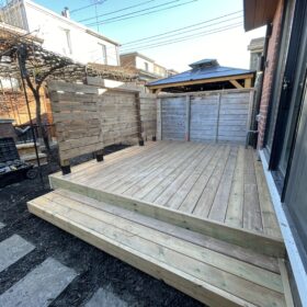 Minimalistic wooden deck in an urban backyard with simple modern furniture and green landscaping.