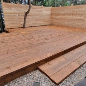 Construction of a new wooden deck in a forested backyard, showing raw timber and tools