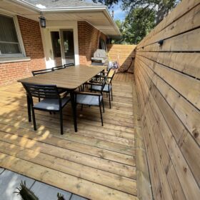 Spacious wooden deck with patio furniture including a table and chairs, surrounded by wooden walls.