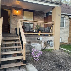 Detailed view of a wooden porch showing sturdy stairs and railings, surrounded by greenery.