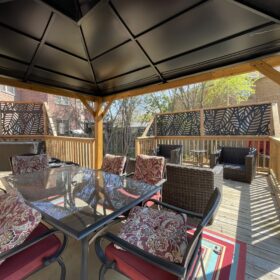 Elegant outdoor dining area under a spacious pergola, surrounded by lush garden and brick walls.