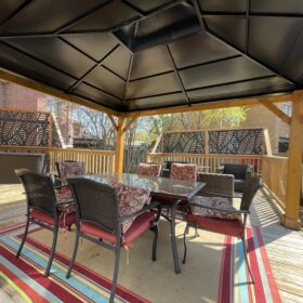 A cozy modern covered patio with a dark retractable roof and stylish outdoor furniture set amidst a residential backdrop.