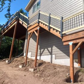 Elevated wooden deck with metal railings attached to a modern grey house