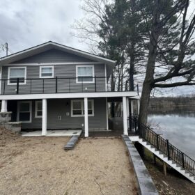 Modern two-story lakeside home with large windows and an extended wooden deck overlooking the serene lake.