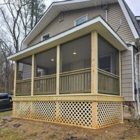 Traditional wooden porch with yellow lattice panels under a covered roof in a forest setting.