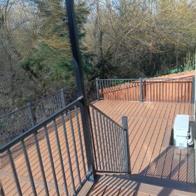 Spacious deck under shade trees with black railings and outdoor furniture