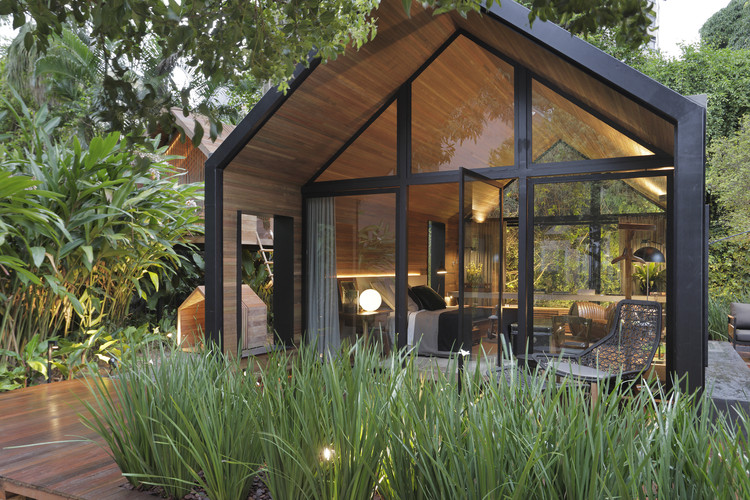 Modern wooden garden house with glass façade and gabled roof surrounded by lush greenery