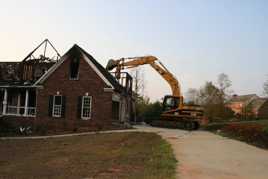 Excavator demolishing a partially burned brick house.