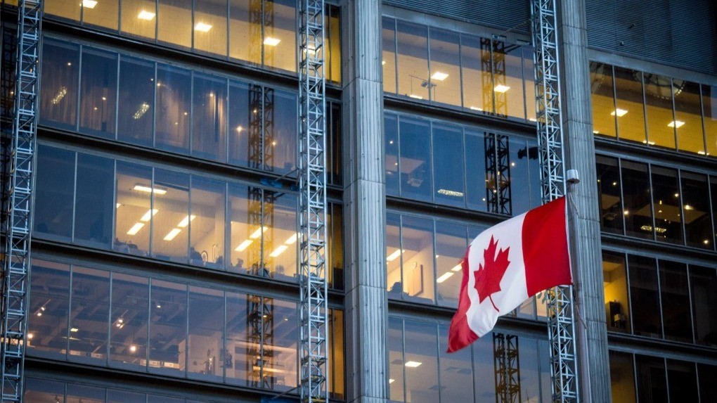 Canadian flag waving in front of a modern glass office building.