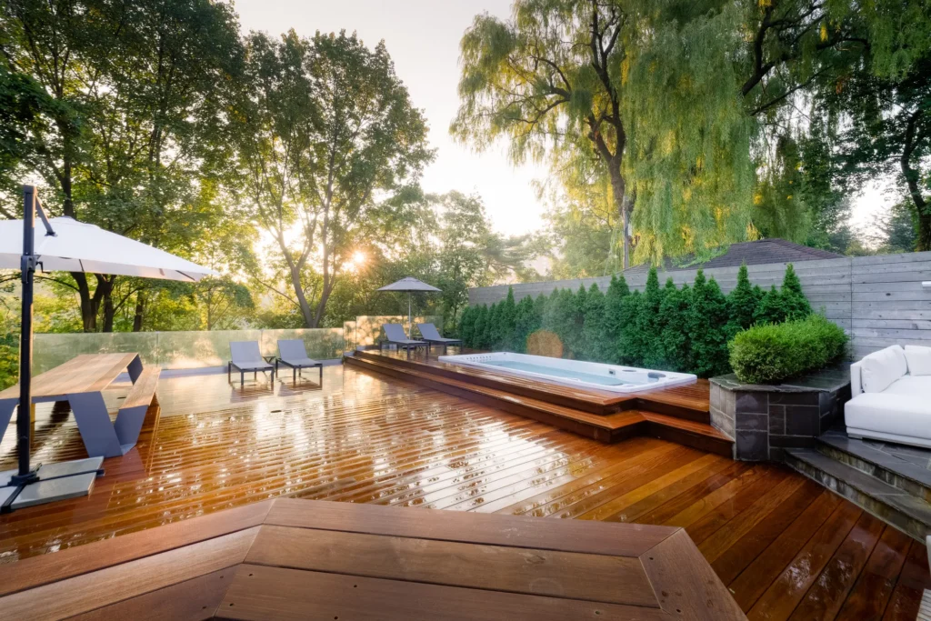 Modern backyard hot tub with wooden deck, surrounded by lush landscaping and stone steps.