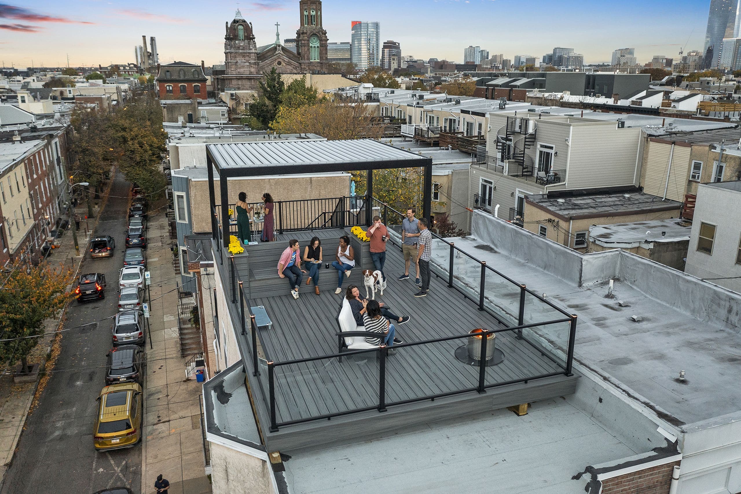 Group of people enjoying a rooftop deck with modern pergola, seating, and city skyline views.