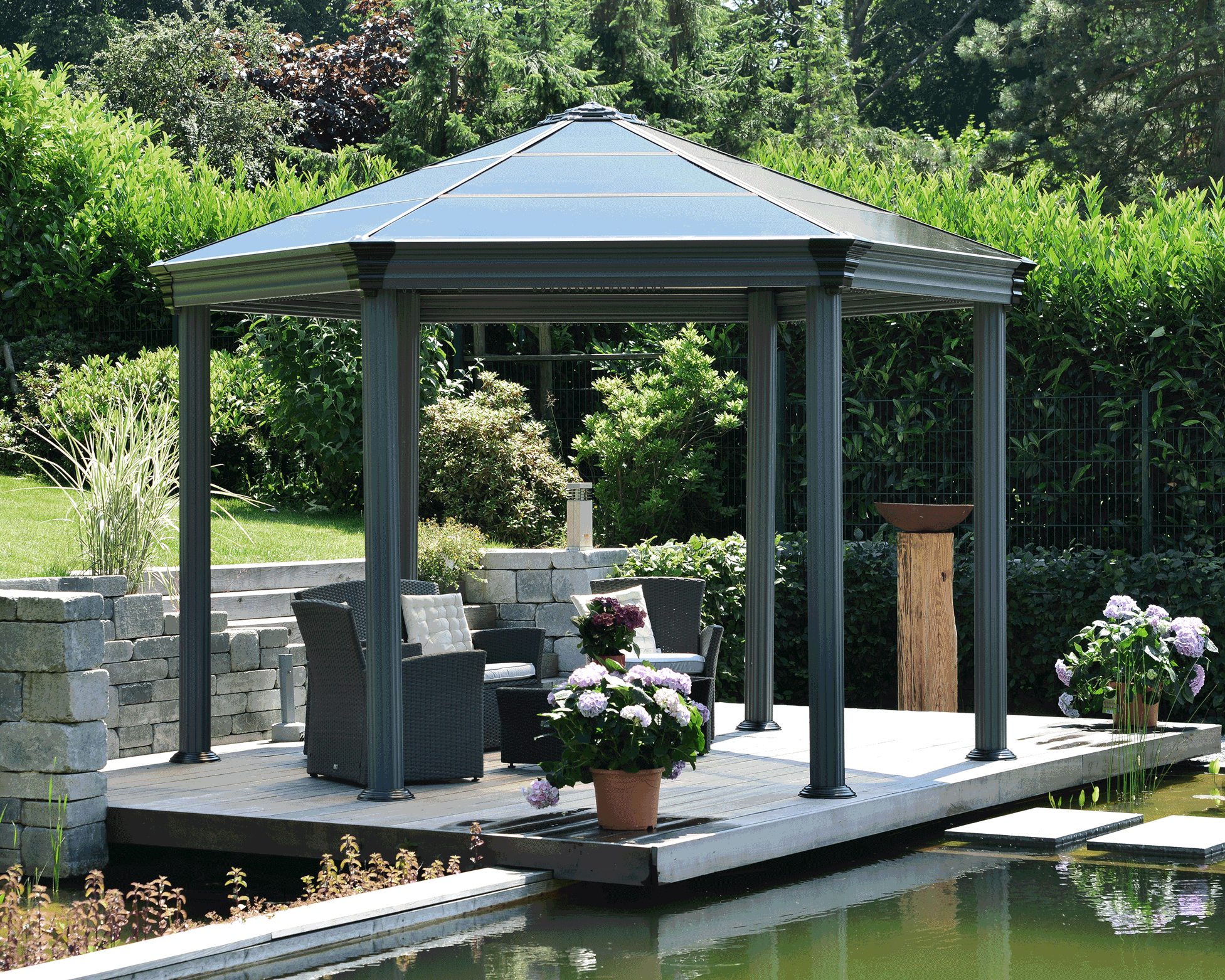 Gazebo with shingled roof in a landscaped garden surrounded by greenery and flowers.