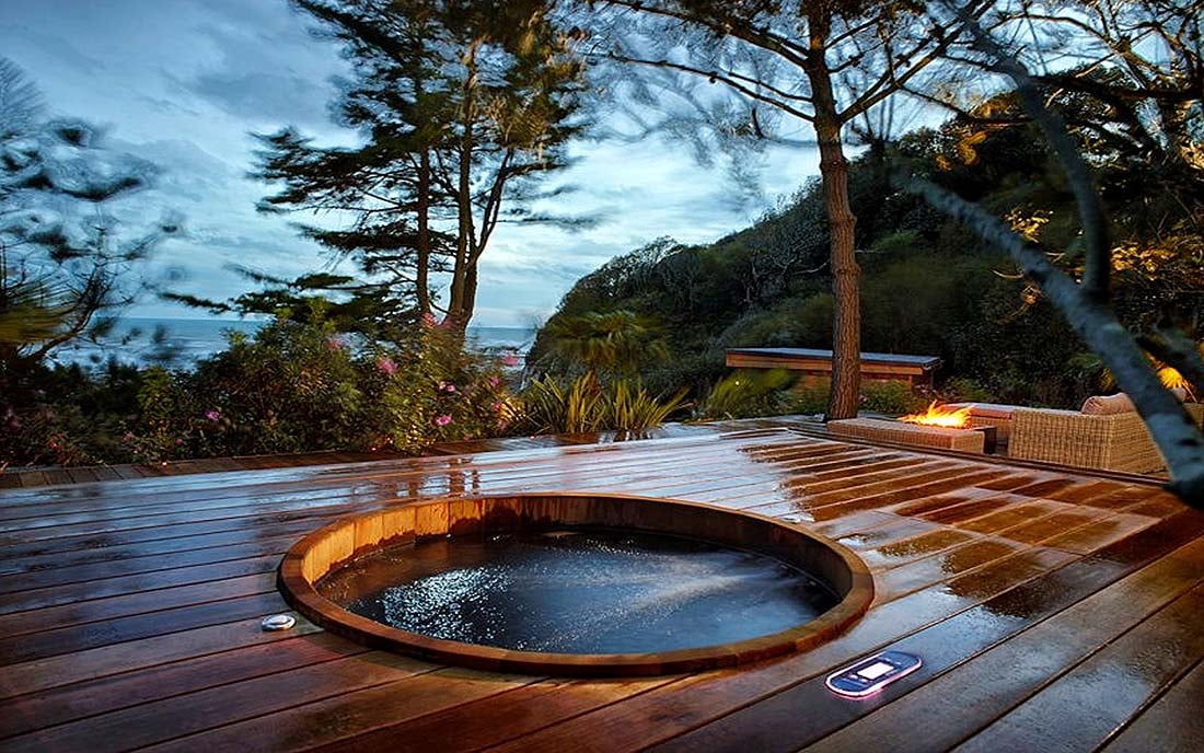 Modern backyard hot tub with wooden deck, surrounded by lush landscaping and stone steps.