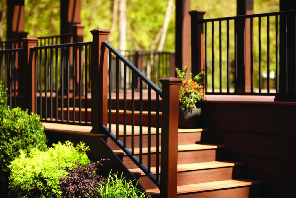 Wood deck stairs with black railing and surrounding greenery
