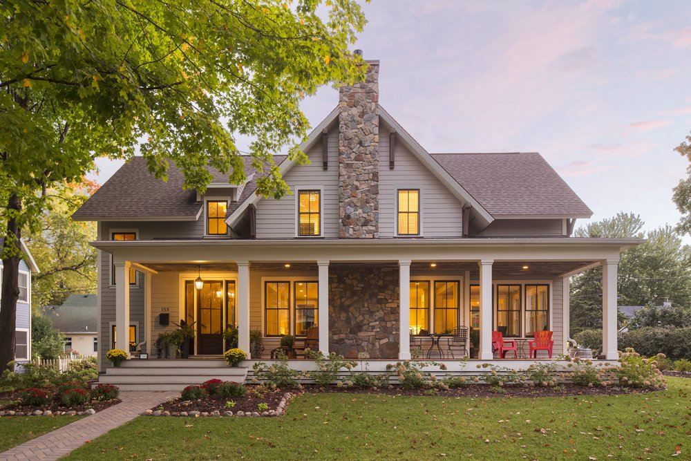 Charming craftsman-style home with stone chimney, large front porch, and warm evening lights.