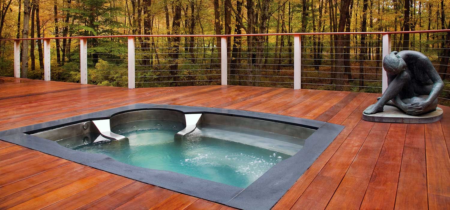 Modern in-ground hot tub with bubbling water built into a wooden deck overlooking a forest.