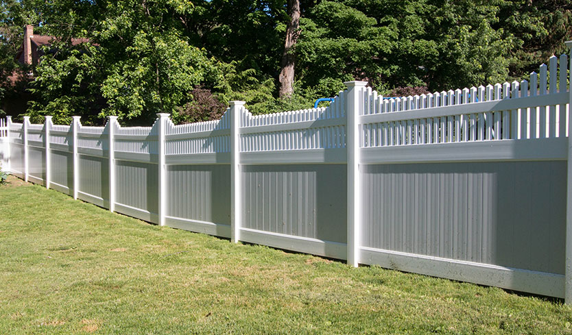 White vinyl privacy fence installed along a backyard lawn.