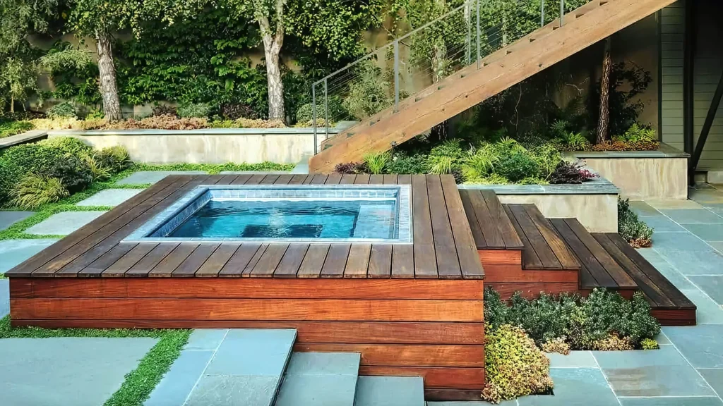 Modern backyard hot tub with wooden deck, surrounded by lush landscaping and stone steps.