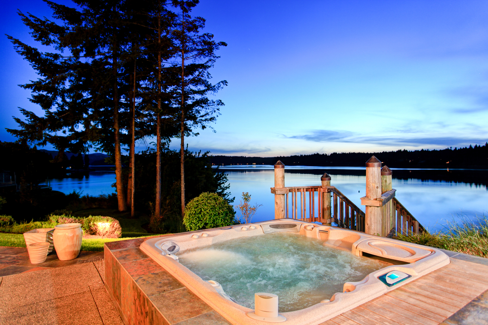 Modern backyard hot tub with wooden deck, surrounded by lush landscaping and stone steps.