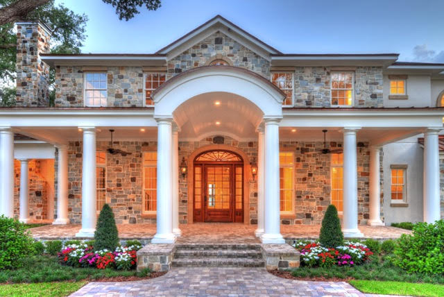 Luxury stone house with grand columns, arched entryway, and landscaped front yard.