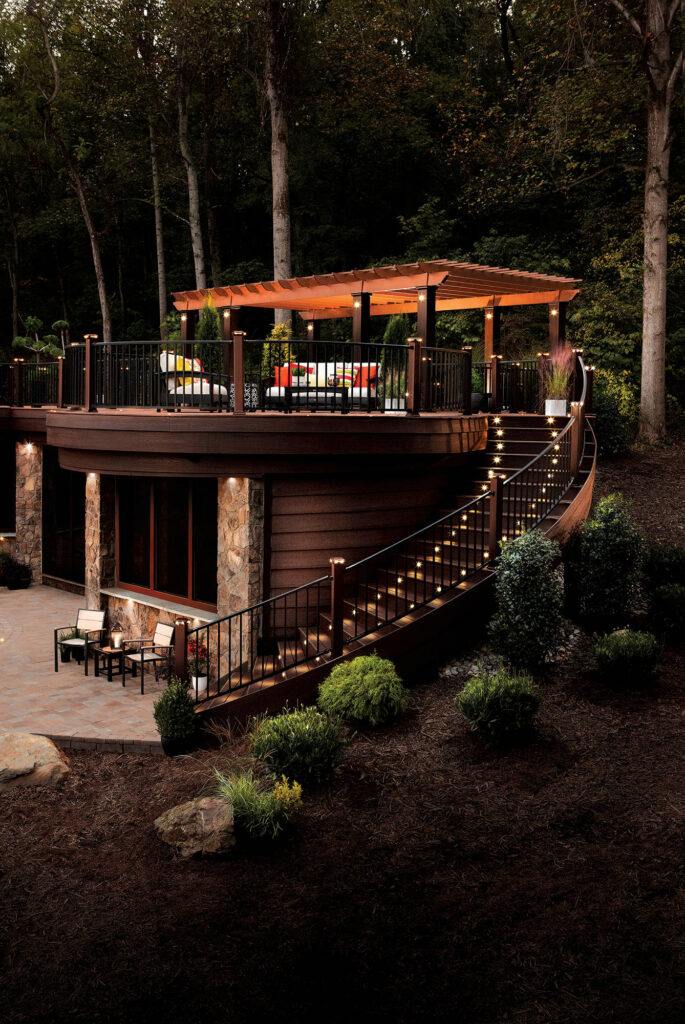 Luxury elevated deck with pergola, modern railing, outdoor seating, and illuminated stairs at dusk.