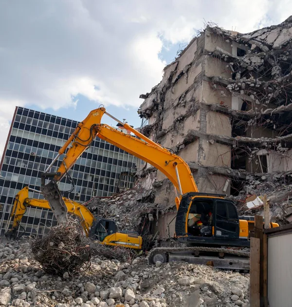 Excavator with hydraulic breaker and skid steer loader at a commercial demolition site.