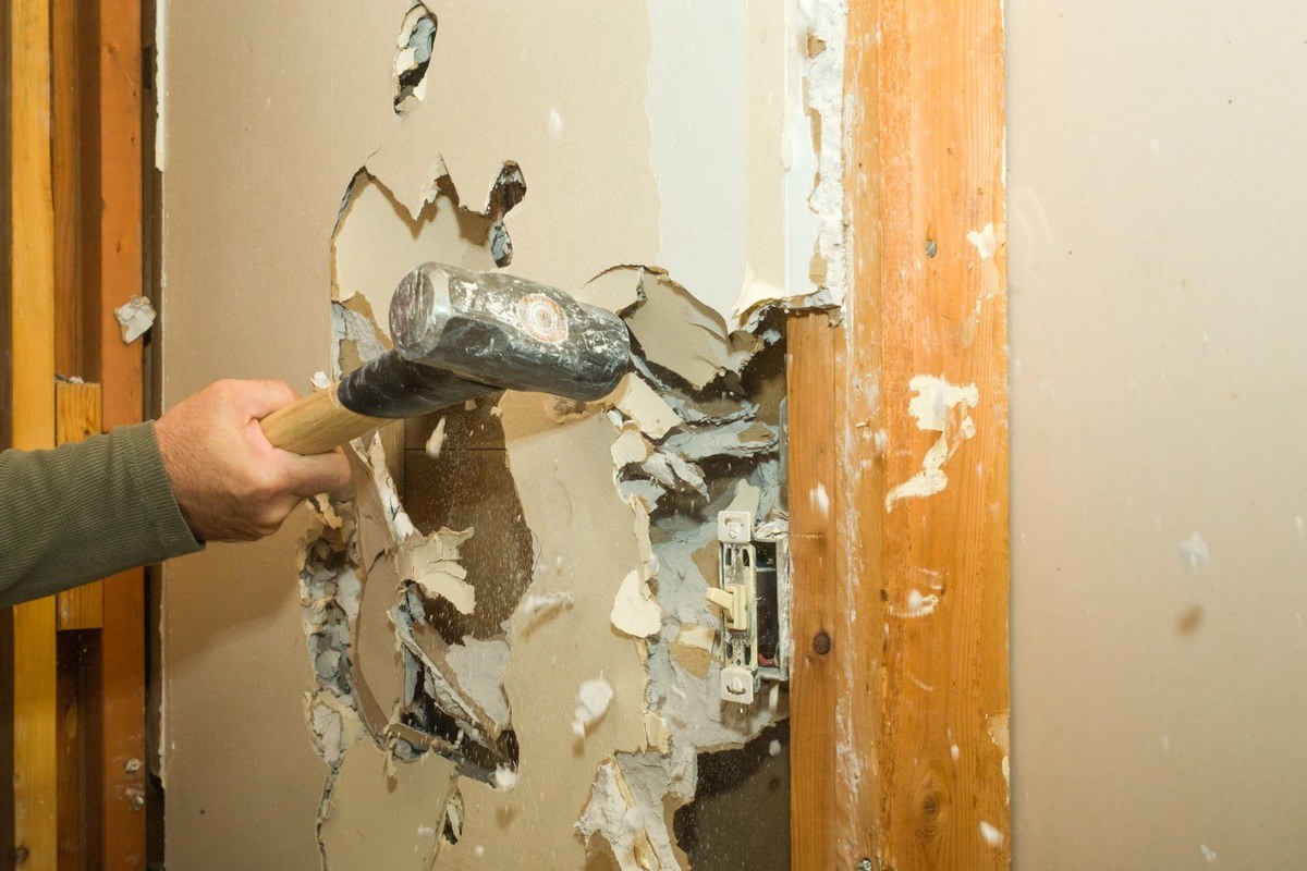 Worker using a sledgehammer to demolish an interior drywall wall.