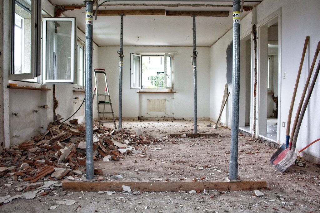 Partially demolished residential interior with debris, exposed supports, and tools.