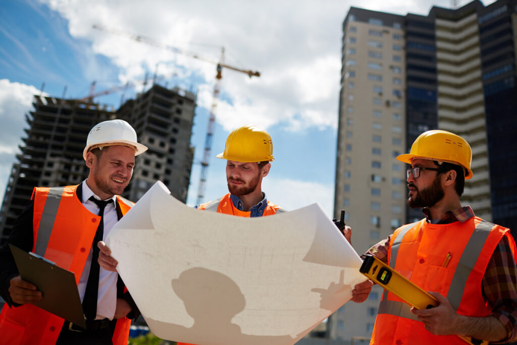 Team of construction inspectors reviewing architectural sketch on paper at a building site.