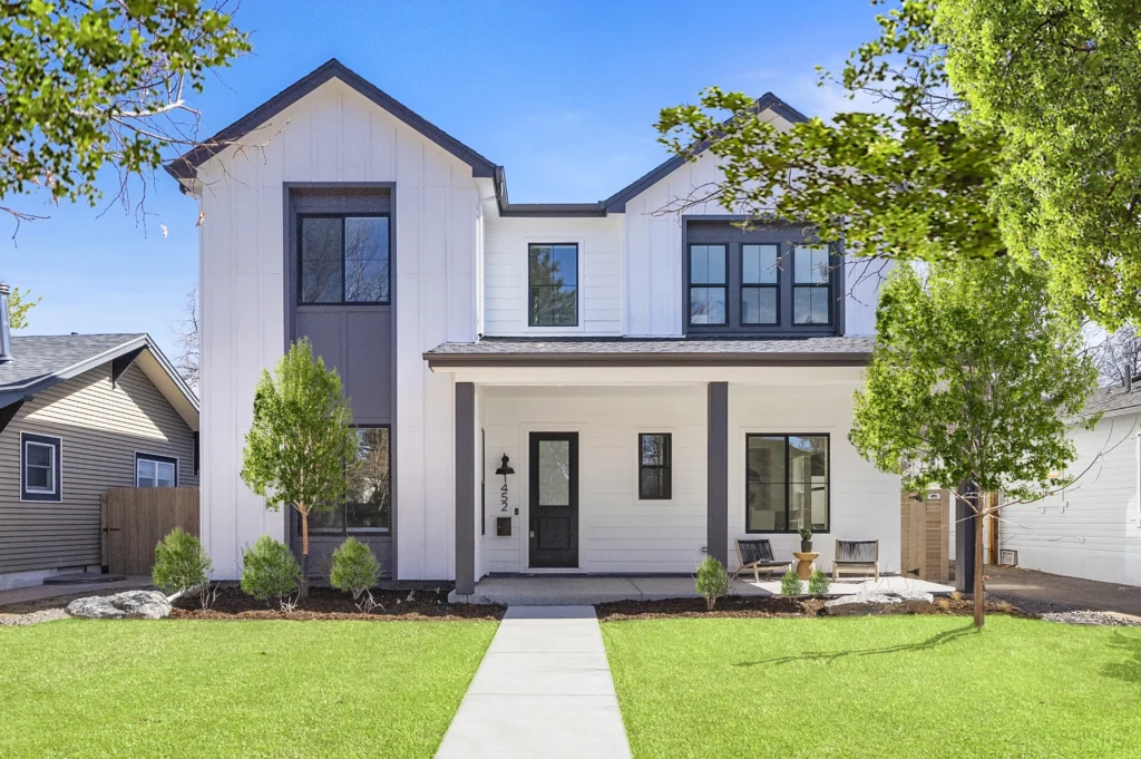 Modern custom-built two-story home with black-trim windows, white siding, landscaped front yard, and covered entry porch.