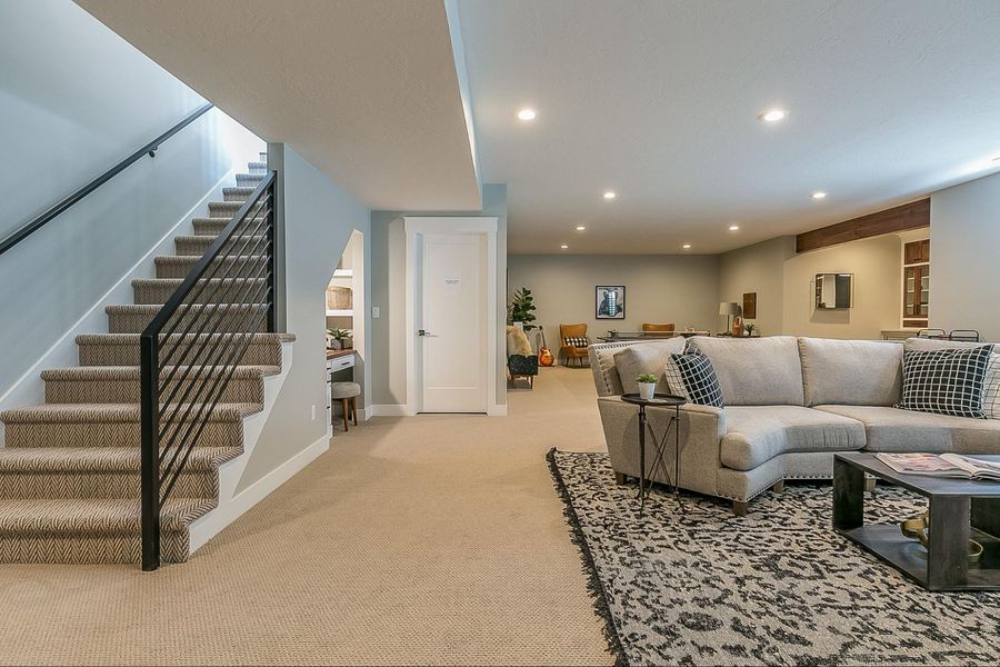 Modern renovated basement with cozy living area, sectional sofa, and carpeted staircase.