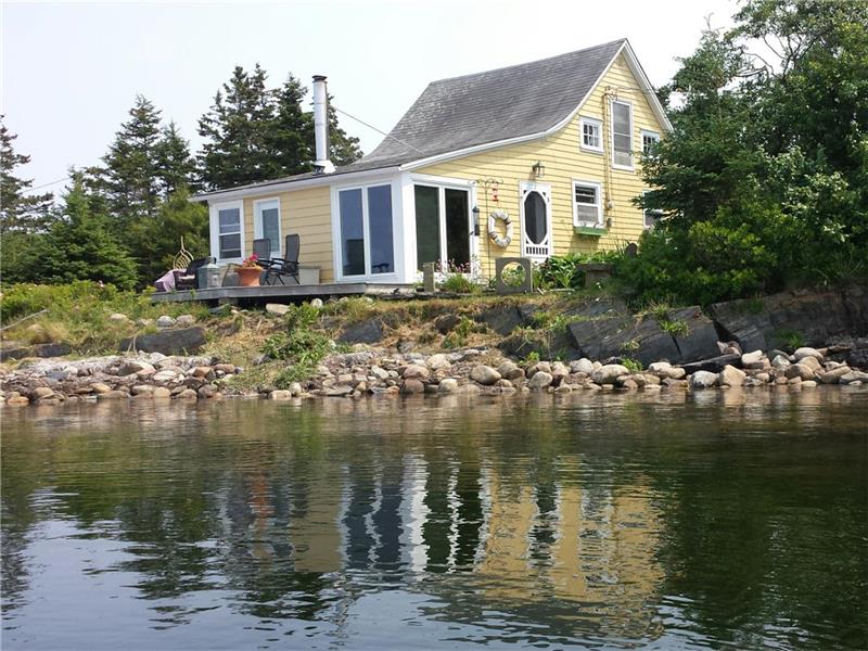 Charming yellow waterfront cottage with outdoor seating, large windows, and scenic lake views.