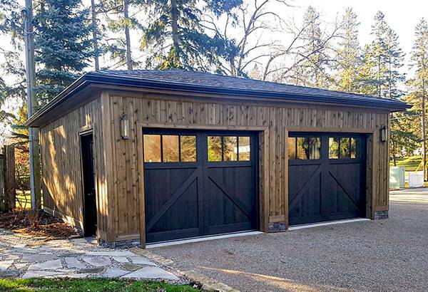 Rustic wooden garage with double black carriage-style doors and exterior lantern lights.