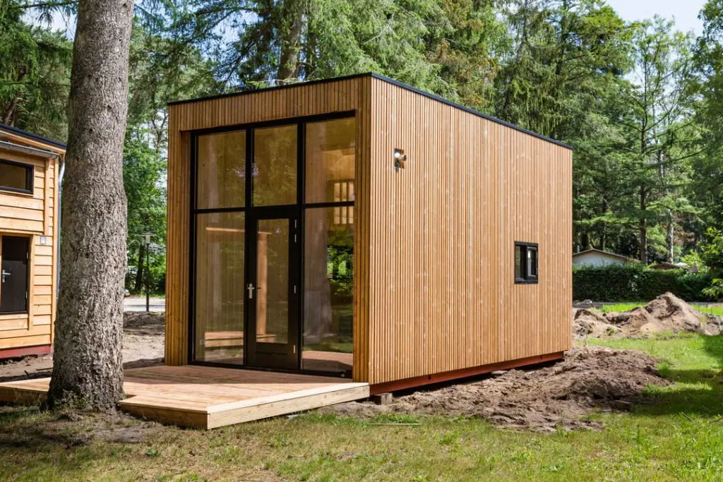 Modern wooden tiny house with floor-to-ceiling glass doors, natural cladding, and forest surroundings.