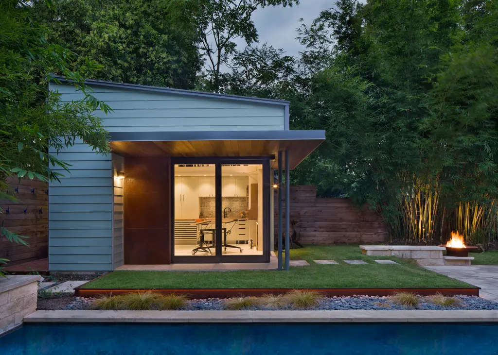 Modern backyard studio with glass doors, sleek design, poolside view, and outdoor fire pit.
