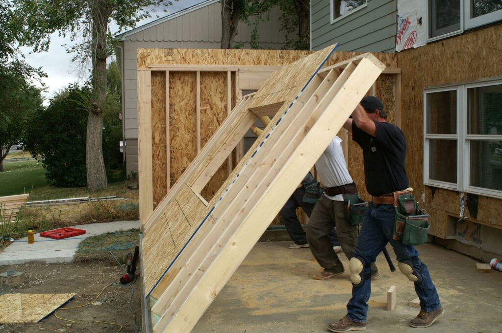 Construction workers lifting and installing a framed wooden wall during a home addition project.