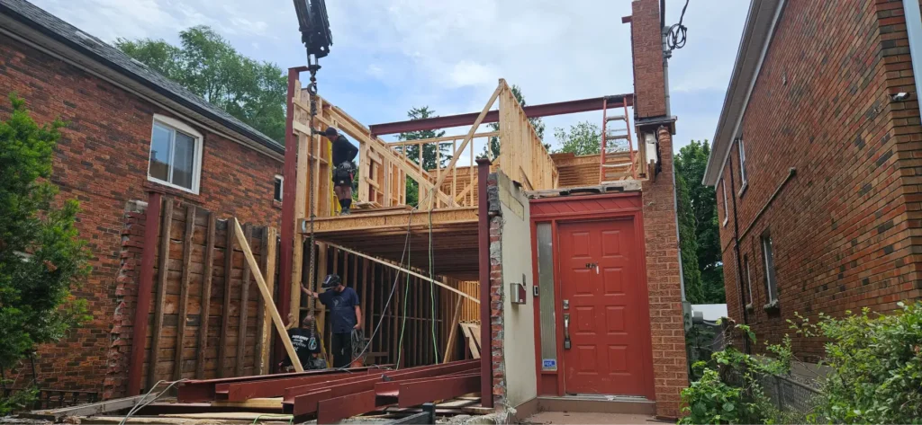 Construction workers building a second-story home addition with wooden framing and steel beams.