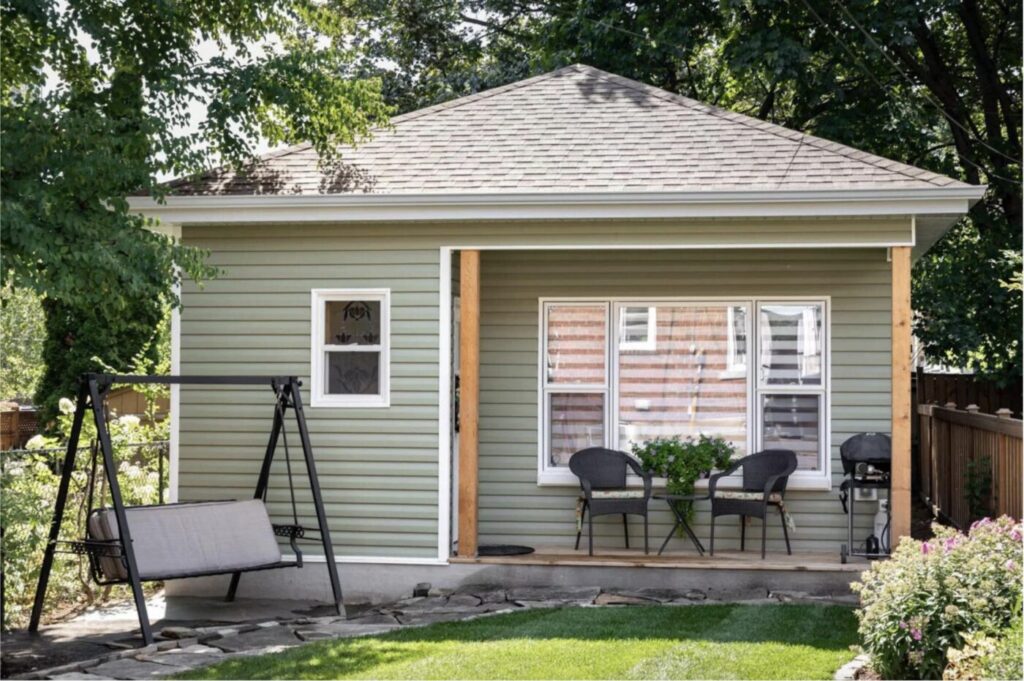 Cozy backyard guest house with green siding, small porch, outdoor seating, and garden swing.