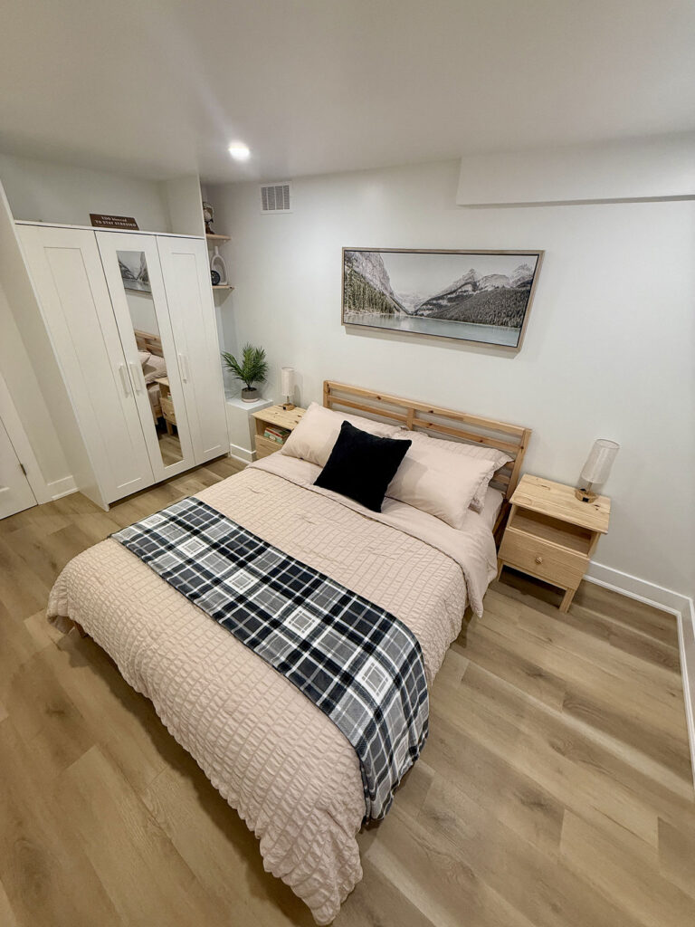 Second bedroom in a finished basement suite with a queen bed, hardwood floors, and natural light in Aurora, ON by Jacko Contracting