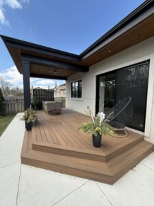 Modern patio with wooden deck, wicker furniture, and potted plants under a clear blue sky. Cozy outdoor relaxation space