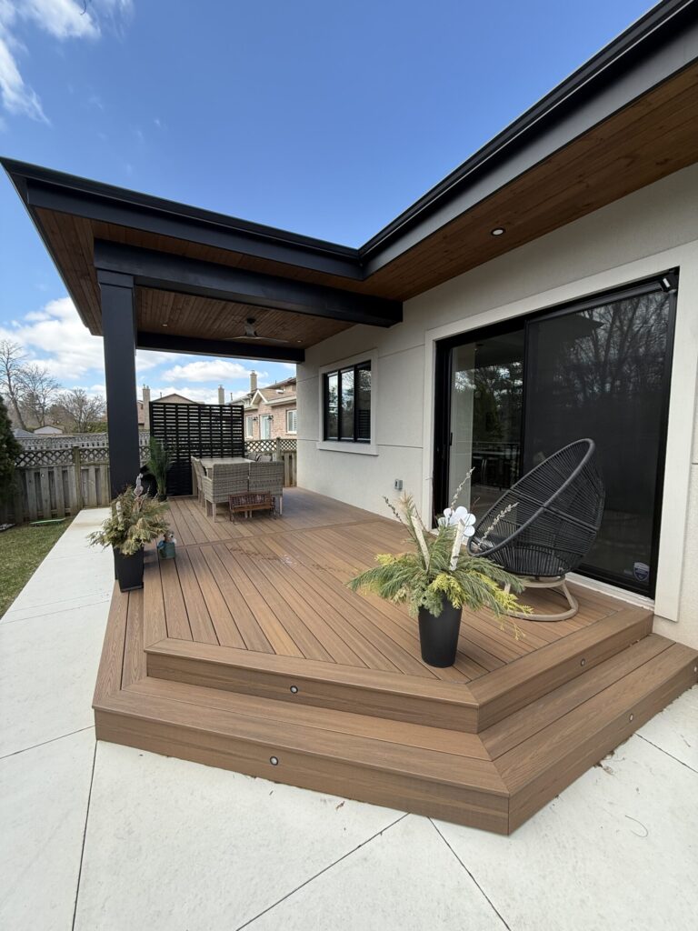 Modern patio with wooden deck, wicker furniture, and potted plants under a clear blue sky. Cozy outdoor relaxation space